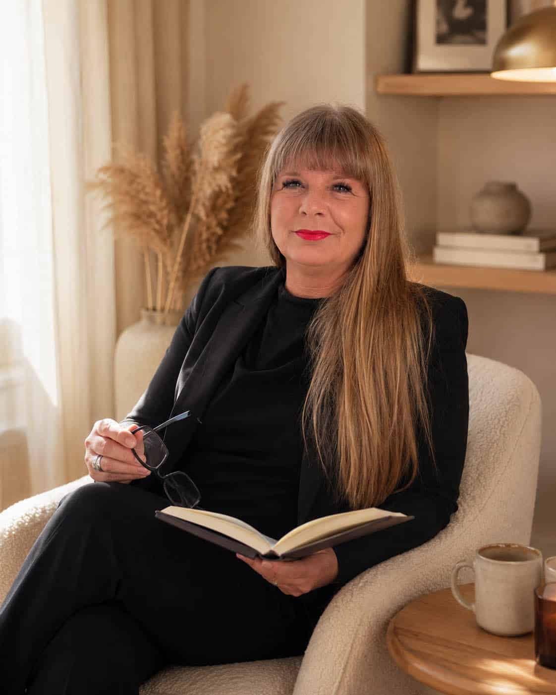 Anette Pelzer sitzt in heller, ruhiger Atmosphäre mit einem Buch und verkörpert den persönlichen Ursprung von Menschenkompass.