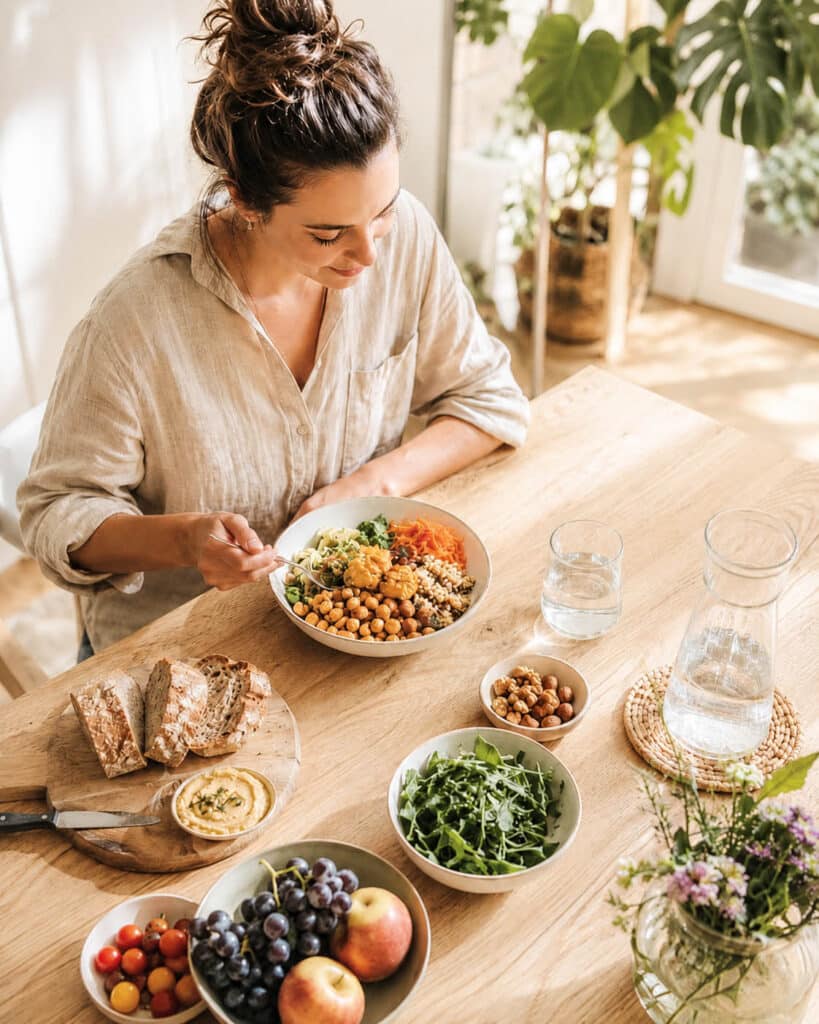Person sitzt an einem hellen Tisch mit einer ausgewogenen Mahlzeit und beschäftigt sich bewusst mit Ernährung, Wohlbefinden und Alltag. Ernährung verstehen